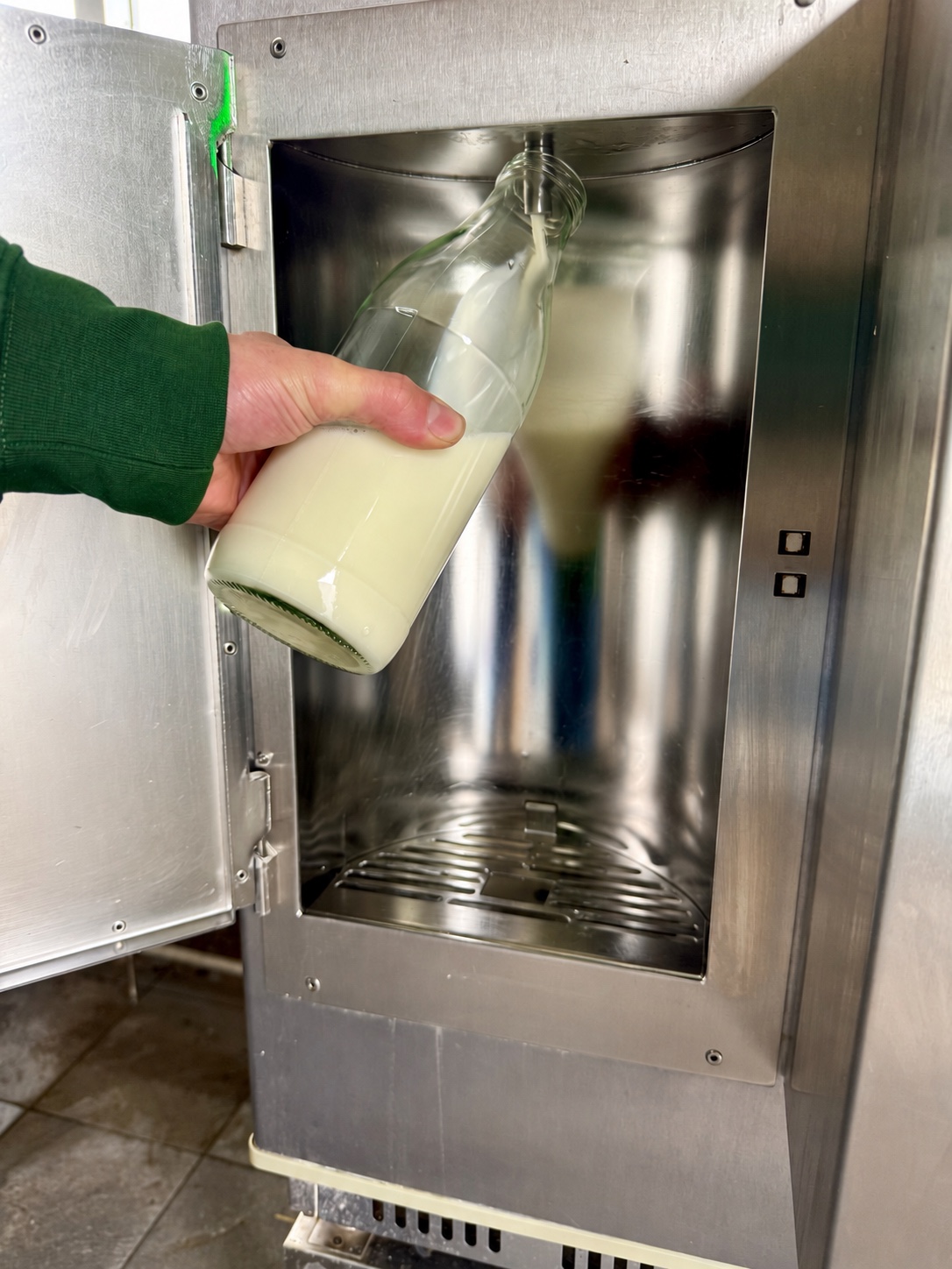 Een glazen fles wordt gevuld met rauwe melk bij de melktap van Hoeve Bouwlust.